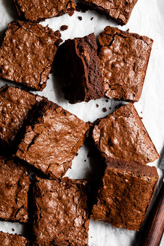 An overhead view of chocolate brownies with a crispy top on parchment paper.