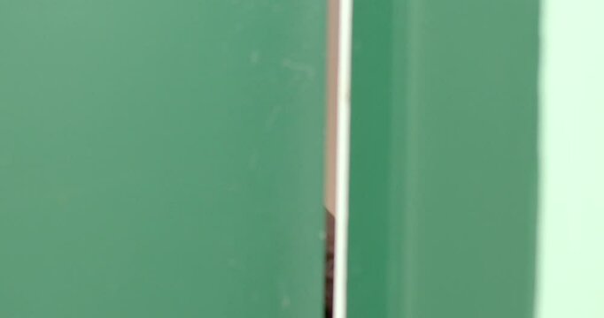A young child is seen peeking intently through a narrow gap in a vibrant green door, capturing a delightful moment filled with curiosity and wonder about what lies beyond