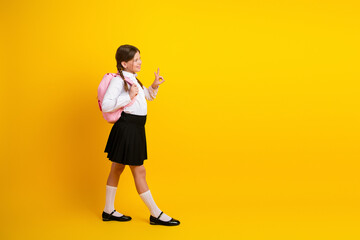 Confident young schoolgirl in uniform with a pink backpack posing on a yellow background, enjoying back-to-school season