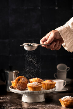 just baked muffins ready for coffee break, woman's hand sifting icing sugar