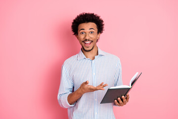 Excited young man reading a book with enthusiasm against a pink background