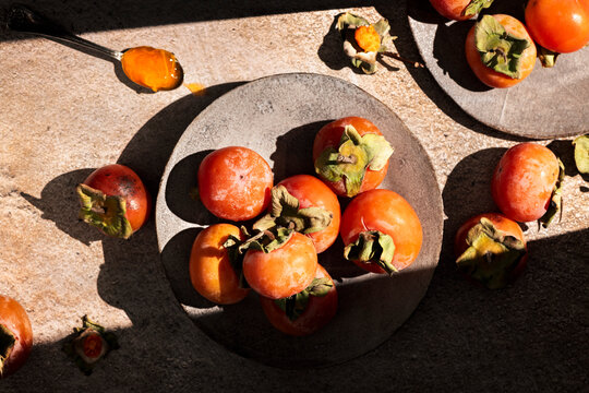 directly above fresh organic persimmon in plates, hard light