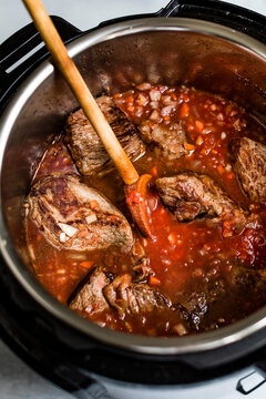 Chunks of beef cooking in a tomato-based sauce inside an electric pressure cooker.