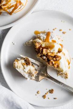 A piece of dessert topped with caramel sauce and nuts on a white plate, with a fork holding a bite-sized portion.