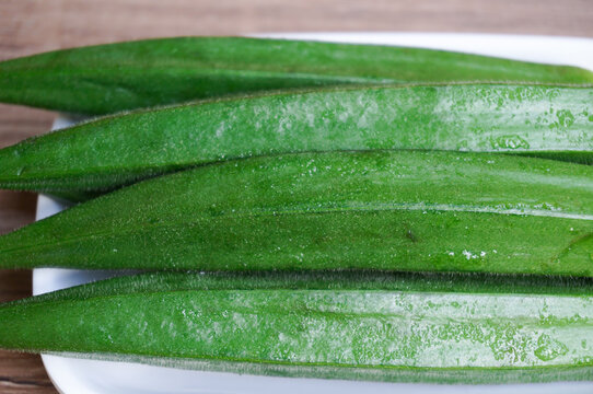 Bendi atau okra Abelmoschus esculentus Moench,lady's fingers,on a white square plate, fresh and organic, wood pattern background,