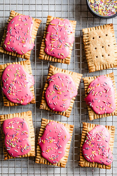 An assortment of rectangular pastries with pink icing and colorful sprinkles on a cooling rack.