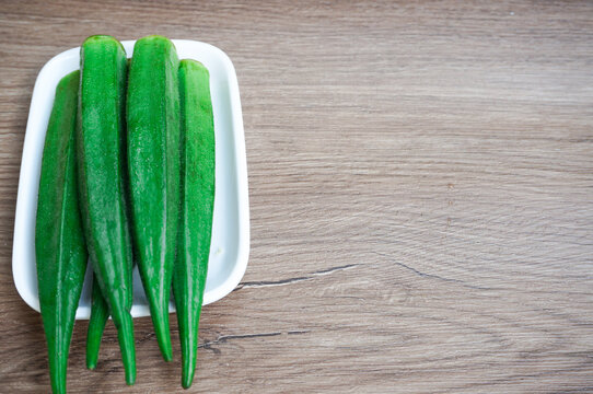 Bendi atau okra Abelmoschus esculentus Moench,lady's fingers,on a white square plate, fresh and organic, wood pattern background,