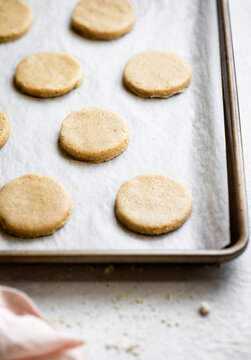 A baking sheet lined with parchment paper holds several round, unbaked cookies.