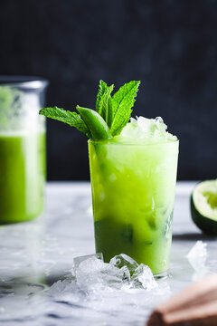 A refreshing green drink with mint leaves and ice cubes on a marble surface.