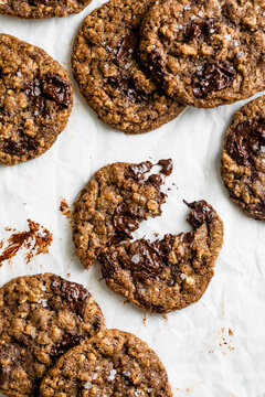 A batch of freshly baked chocolate chip cookies with a chewy texture and visible sea salt flakes, arranged on parchment paper.