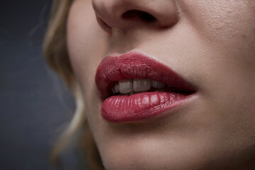 Fototapeta premium Fragment of a woman's face with lips painted with red lipstick.
