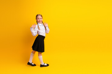 Happy student in uniform smiling on yellow background showing playful gesture with hands, representing education and fun