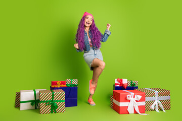 Cheerful young woman with vibrant style posing joyfully with gift boxes on a bright green...