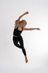 Fototapeta premium Dancer Toni in the studio dancing with motion and light - The image depicts a dancer captured mid-air in a striking pose. They are dressed in a black tank top and black leggings