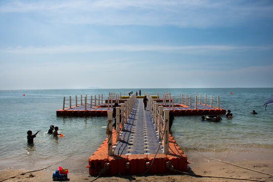 Thai people and foreign travelers travel visit play sand and swimming wave water in sea with plastic pontoons pier ocean of Bangsaen Beach at Chon Buri city on November 8, 2022 in Chonburi, Thailand