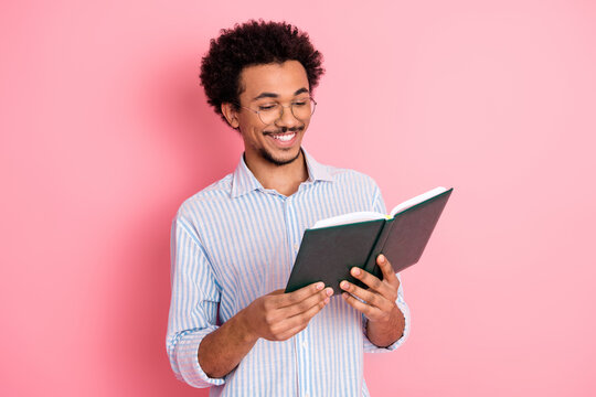 Young stylish man reading a book with a cheerful expression against a vibrant pink background