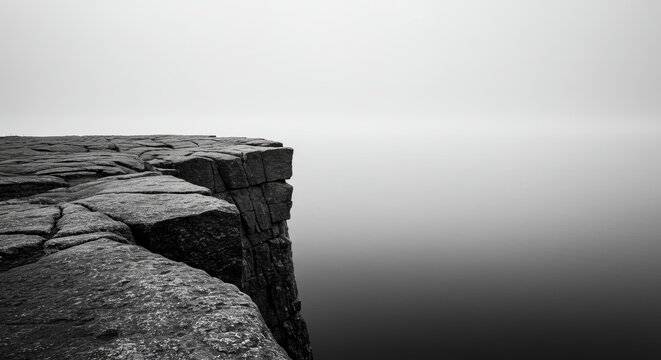 Serene monochrome landscape featuring a rugged cliff edge merging into sea mist