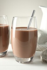 Tasty chocolate milk in glasses on white wooden table, closeup