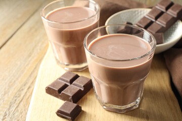 Tasty chocolate milk in glasses and pieces on wooden table, closeup