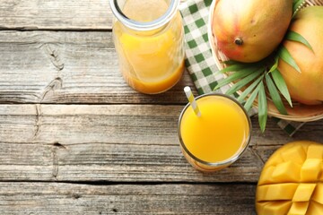 Tasty mango juice in glass, carafe, fresh fruits and leaves on wooden table, flat lay. Space for...
