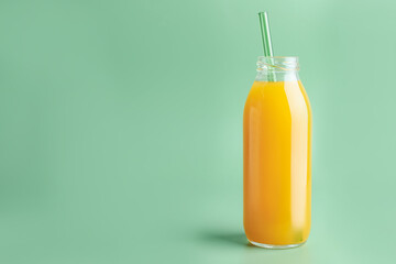 Tasty mango juice in glass bottle on green background, space for text