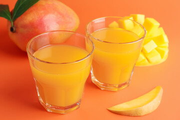 Tasty mango juice in glasses and fresh fruits on orange background, closeup