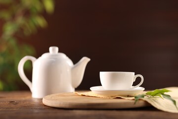 Cup of tasty tea, teapot and leaves on wooden table