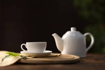 Cup of tasty green tea, teapot and leaves on wooden table