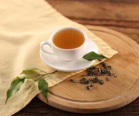 Cup of tasty green tea and leaves on wooden table