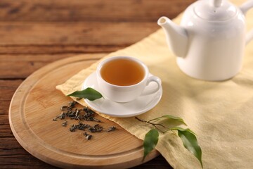 Cup of tasty green tea, teapot and leaves on wooden table