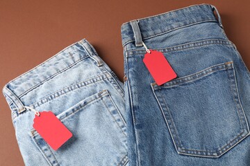 Jeans with tags on brown background, top view