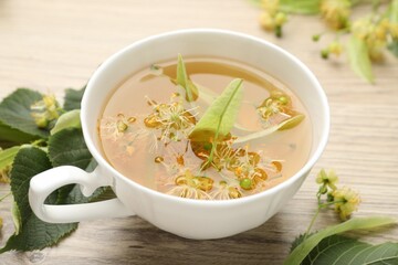 Fresh linden tea in cup and flowers on wooden table, closeup