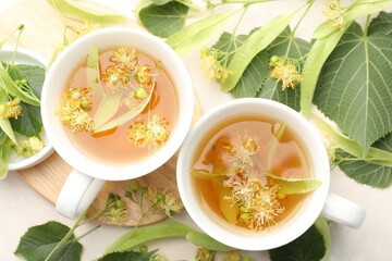 Fresh linden tea in cups and flowers on white table, flat lay