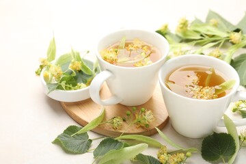 Fresh linden tea in cups and flowers on white table, closeup