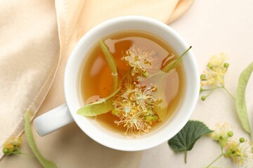 Fresh linden tea in cup and flowers on white table, flat lay