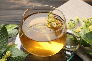 Fresh linden tea in cup and flowers on dark wooden table, closeup