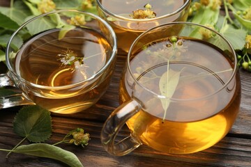 Fresh linden tea in cups and flowers on wooden table, closeup