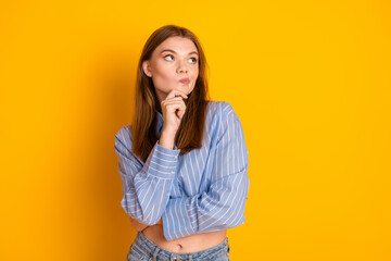 Young woman with thoughtful expression posing against a vibrant yellow background in casual and...