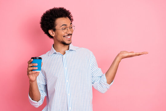 Cheerful young male student holding a coffee cup and gesturing with confidence against a vibrant pink background
