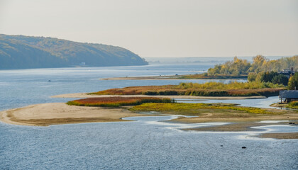 Scenic landscape view of Volga river, sandy beach, golden green vegetation, calm water, background of scenery hills and a green island. Cloudless sky. Kazan, Upper Uslon, Tatarstan, Russia