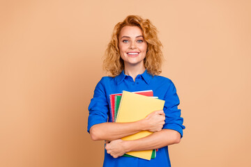 Confident young woman holding colorful notebooks smiling in a vibrant casual outfit against a beige...