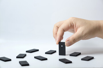 Hand arranging a domino piece within scattered tiles on a plain white surface, portraying concepts of strategy, decision-making, and sequencing processes.