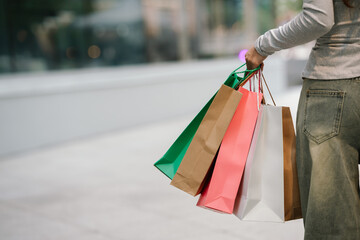 A person in jeans and a long-sleeved shirt carries several colorful shopping bags, likely after a...