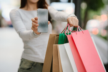 A person in jeans and a long-sleeved shirt carries several colorful shopping bags, likely after a...