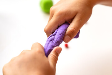 Kid pulling and stretching purple modeling clay. Educational summer holiday activity supporting creativity and motor skills. Bright colors and selective focus.