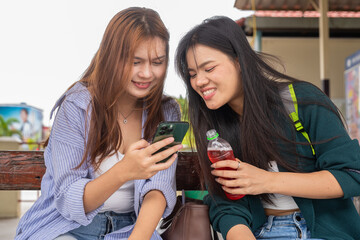 Two young women at train station sitting drinking and using mobile phone