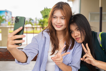 Two young women influencers at train station sitting drinking and using mobile phone taking selfie