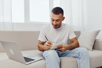 Smiling man writing notes with a laptop nearby, showcasing modern workspace vibes and creativity....