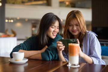 two women drinking coffee in cafe and using phone