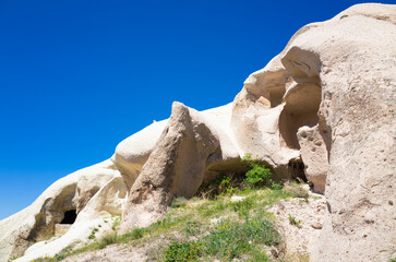 Natural rock formations with ancient cave dwellings carved into soft tuff rock in Cappadocia, Turkey. Scenic summer landscape of Cappadocia with arid terrain, bright blue sky and sparse vegetation.